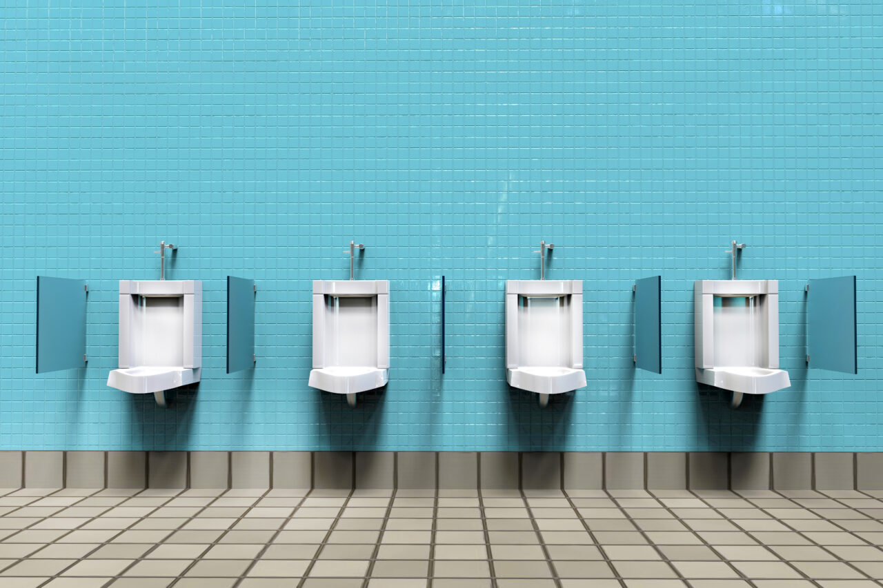 Modern mens restroom with four clean white porcelain urinals aligned against a blue tiled wall.