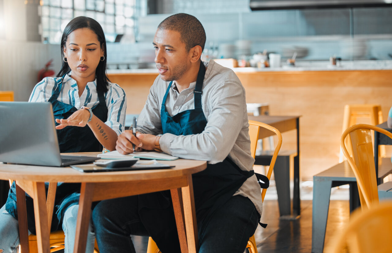 Two people in aprons discuss work at a laptop, exemplifying service connecting manufacturers and end users.