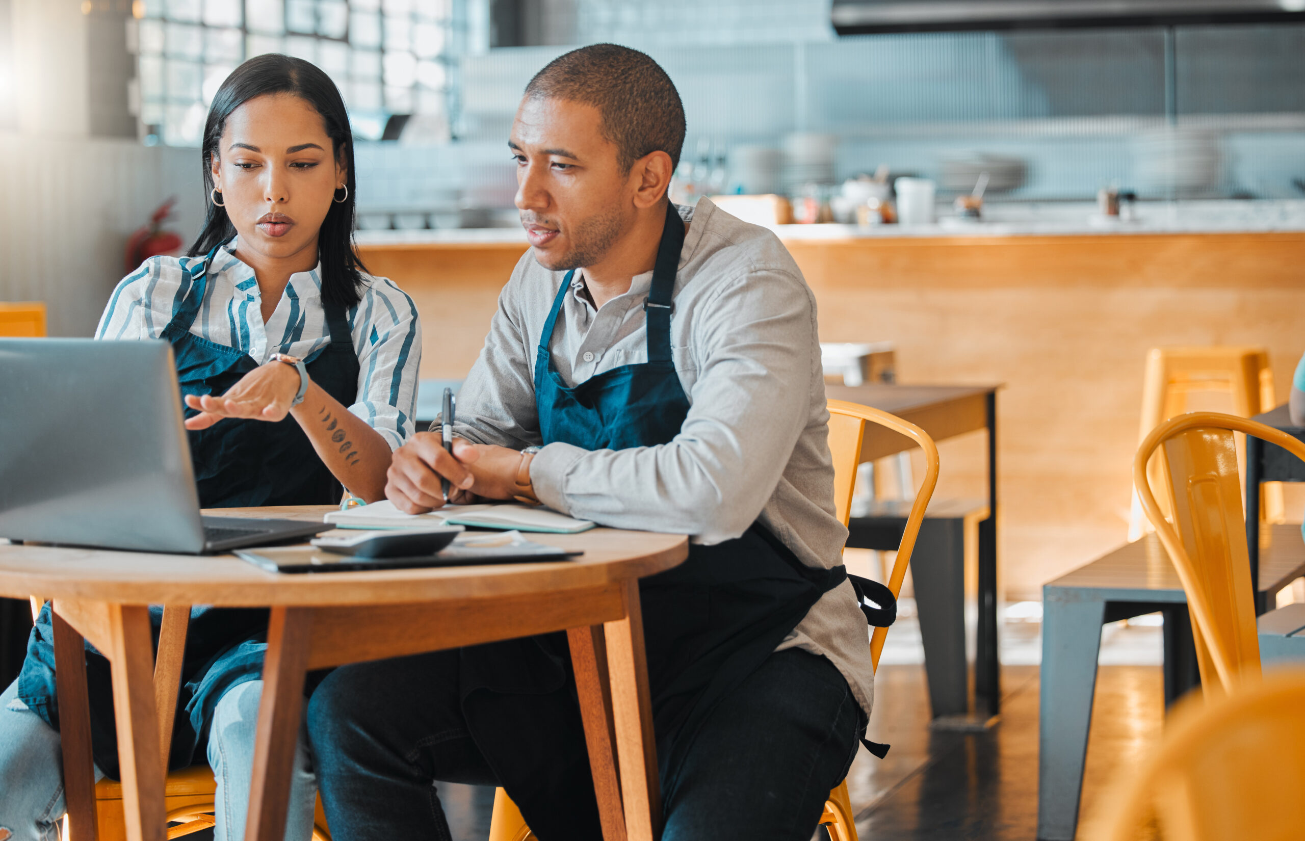 Two people in aprons discuss work at a laptop, exemplifying service connecting manufacturers and end users.