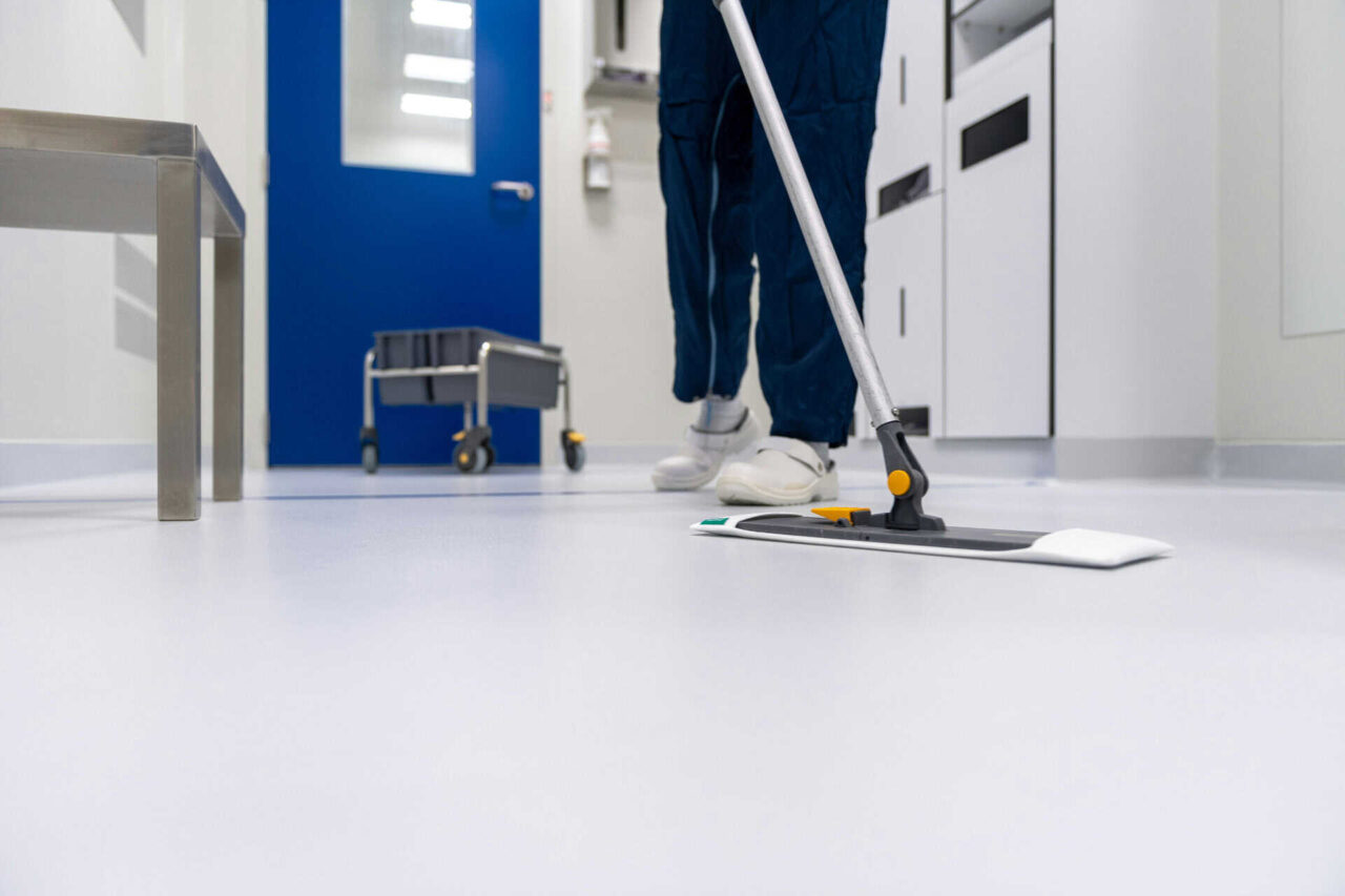 Person mopping a clean facility floor with janitorial supplies, emphasizing facility solutions efficiency.