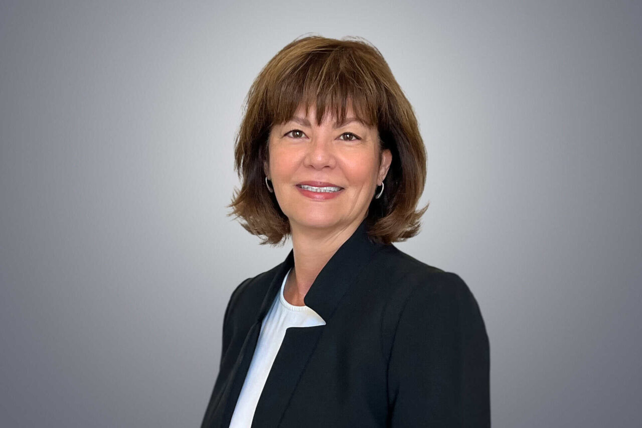 Professional woman smiling, wearing a black blazer, symbolizes helping manufacturers and end users grow.