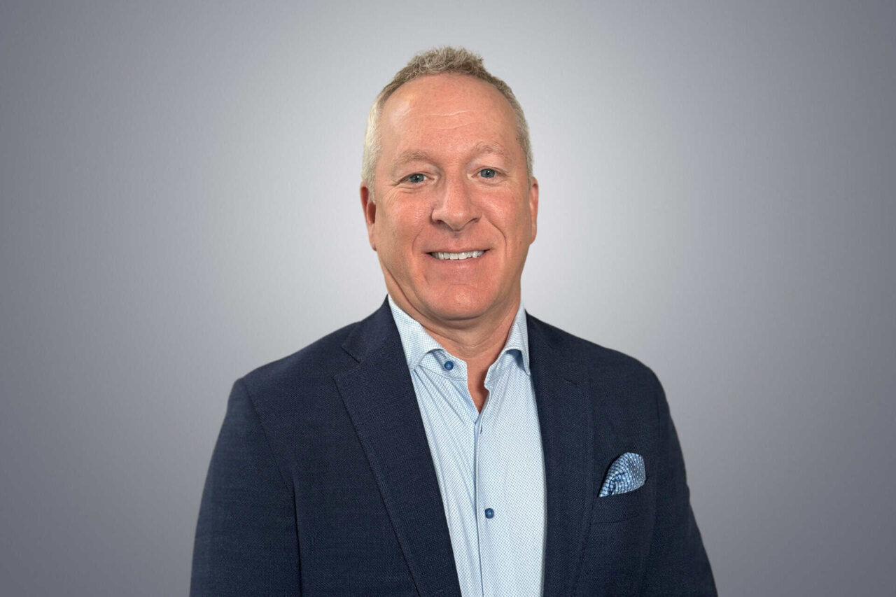 Professional man in a suit smiling, representing leadership in helping manufacturers, distributors, and end users grow.