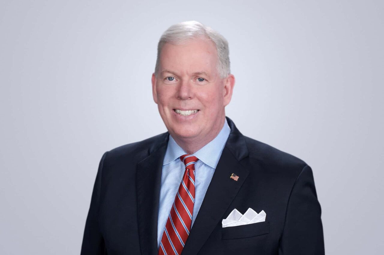 Smiling professional in a suit with a red tie, symbolizing connections in helping manufacturers, distributors, and end users grow.
