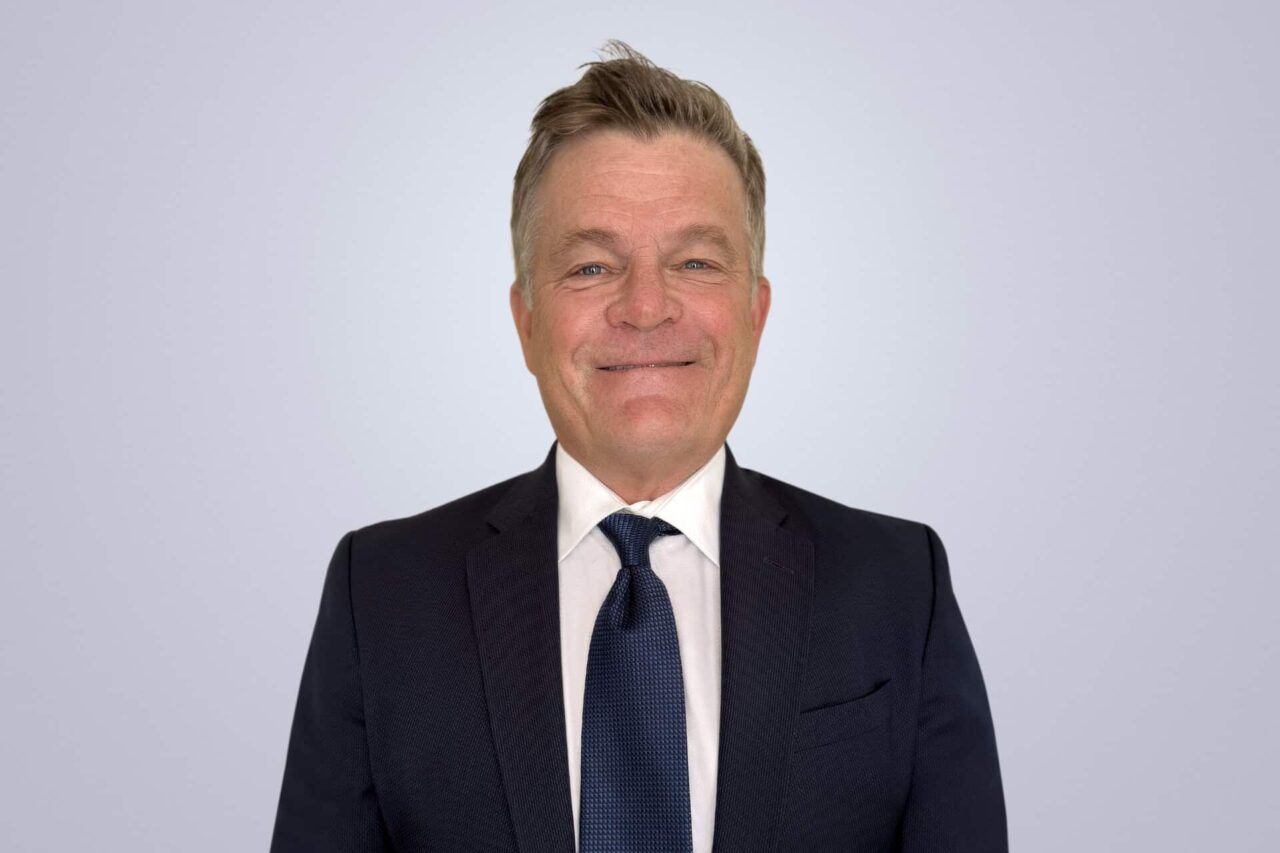Smiling professional man in a suit, representing helping manufacturers, distributors, and end users grow.