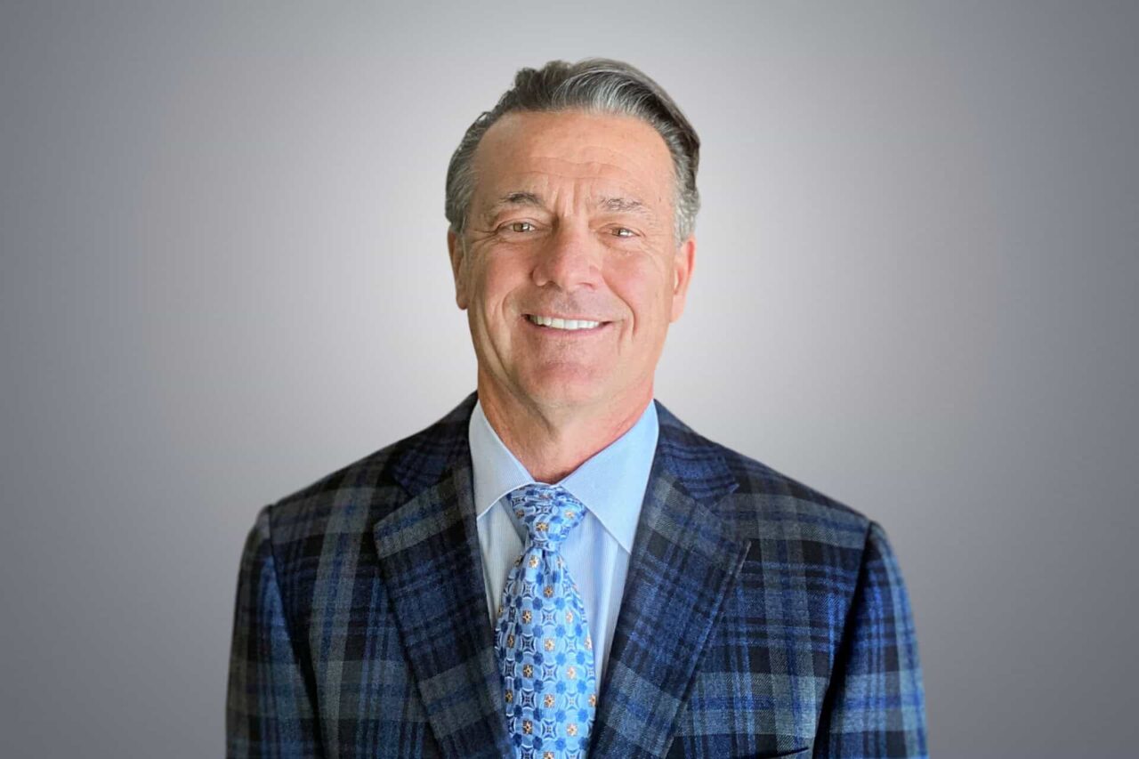 Smiling man in a plaid blazer and patterned tie, representing helping manufacturers and users grow.