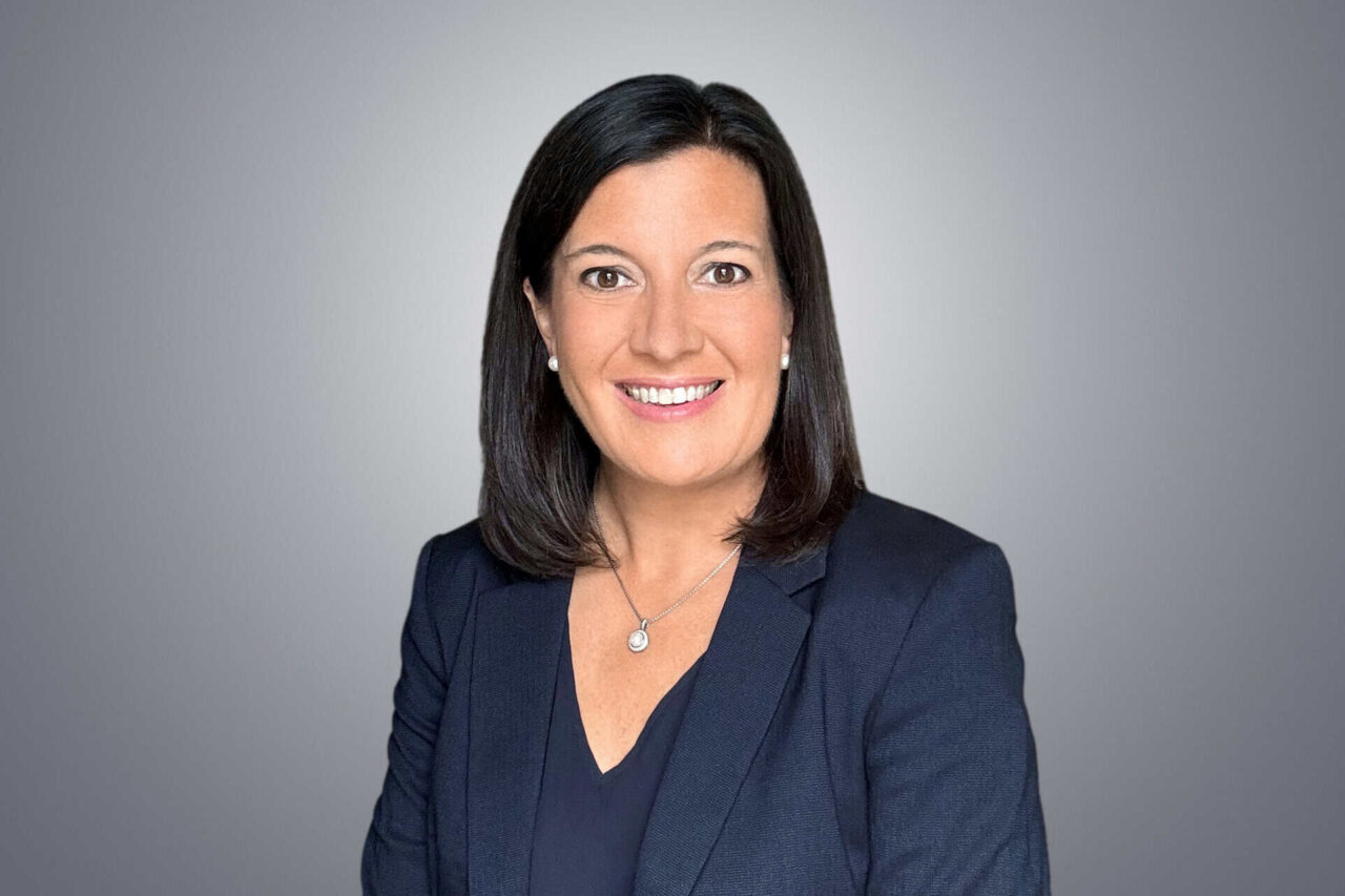 Professional woman in a dark blazer smiling, representing helping manufacturers, distributors, and end users grow.