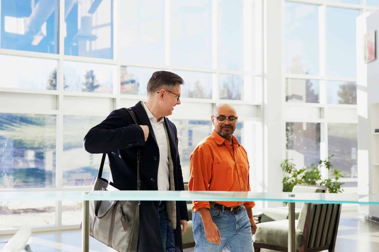 Two men walking in a bright office, discussing food service supply and expanding manufacturer reach.