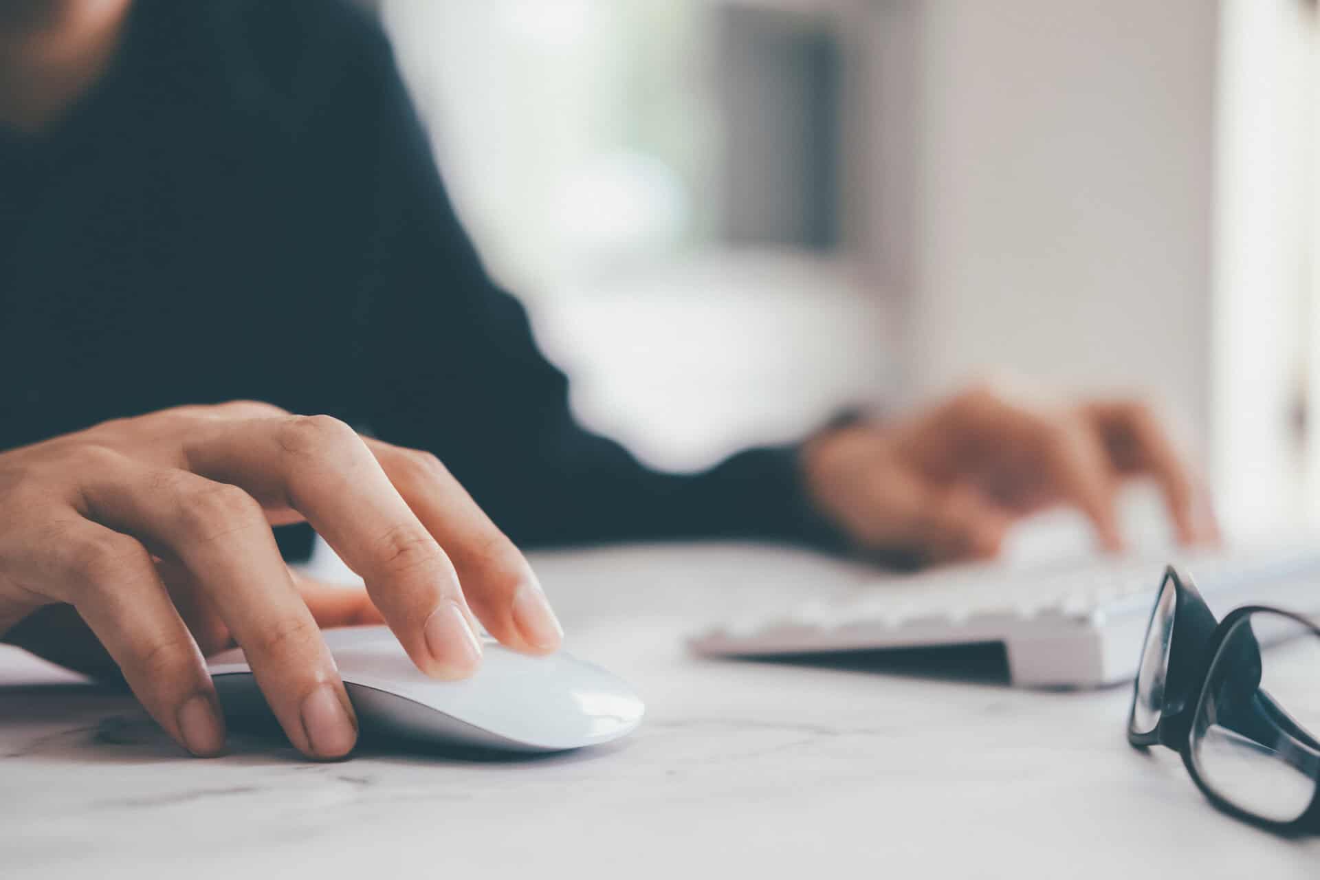 Hand using a computer mouse beside glasses, highlighting expertise help and product expertise for distributors.