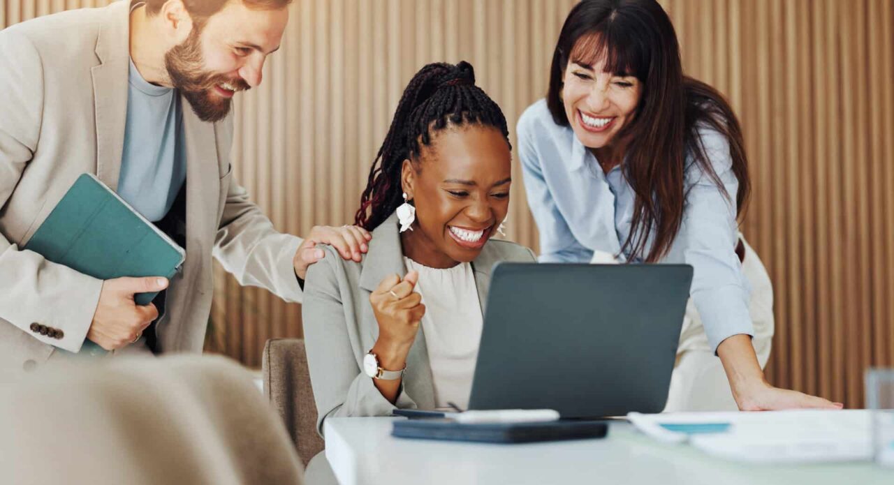 Smiling team around a laptop celebrates success, reflecting manufacturers representative expanding growth.