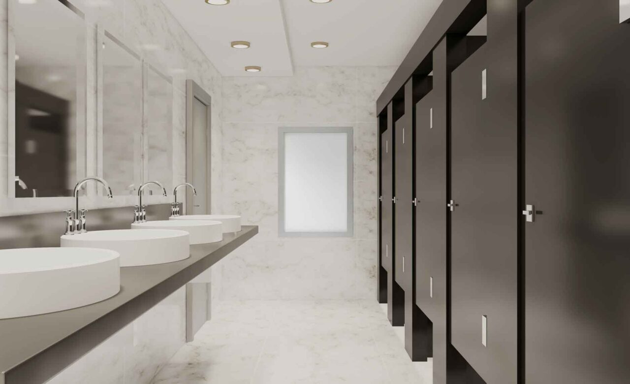 Modern restroom with marble walls, row of sinks, and dark stall doors, showcasing trusted janitorial solutions.