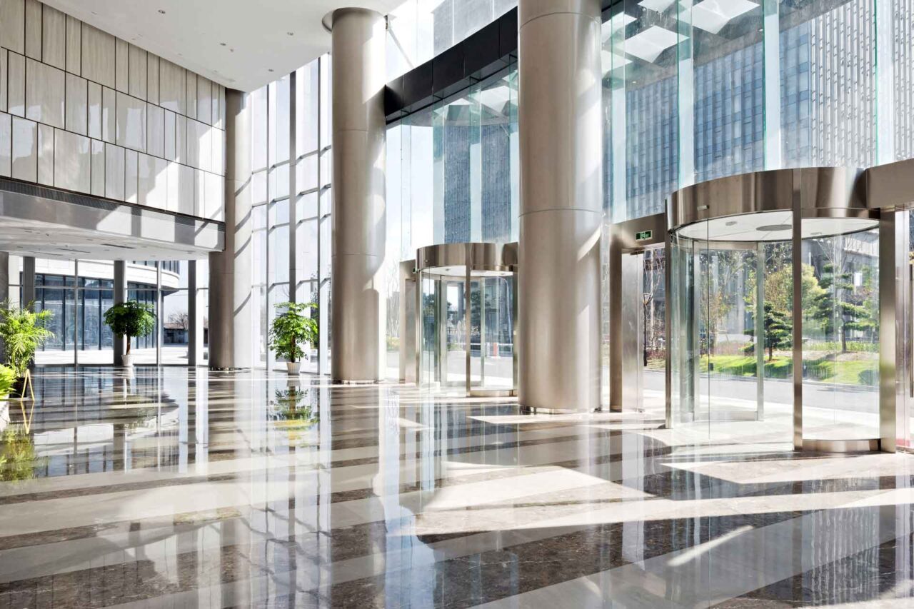 Spacious modern lobby with glass walls and revolving doors, showcasing trusted janitorial solutions for end users.