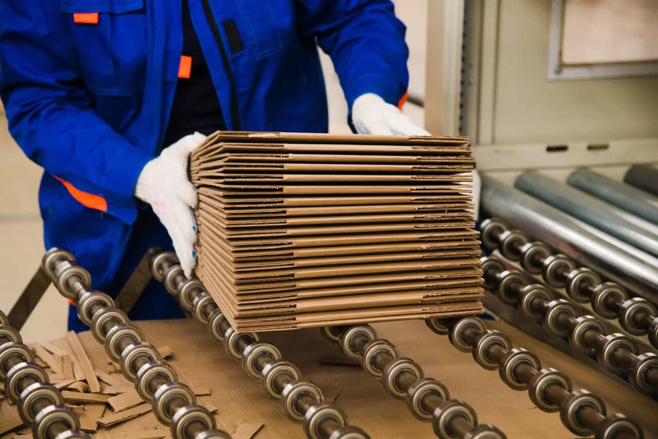 Worker in blue uniform handling cardboard sheets on a conveyor, enhancing packaging manufacturers' service supply.