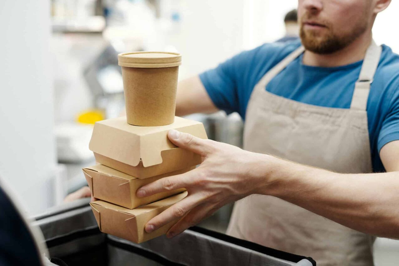 Man stacking biodegradable food containers and cup, showcasing food service supplies in packaging industry.