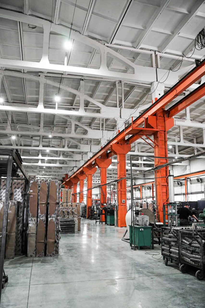 Industrial warehouse interior with orange beams, packaging materials, and workers enhancing manufacturers' reach.