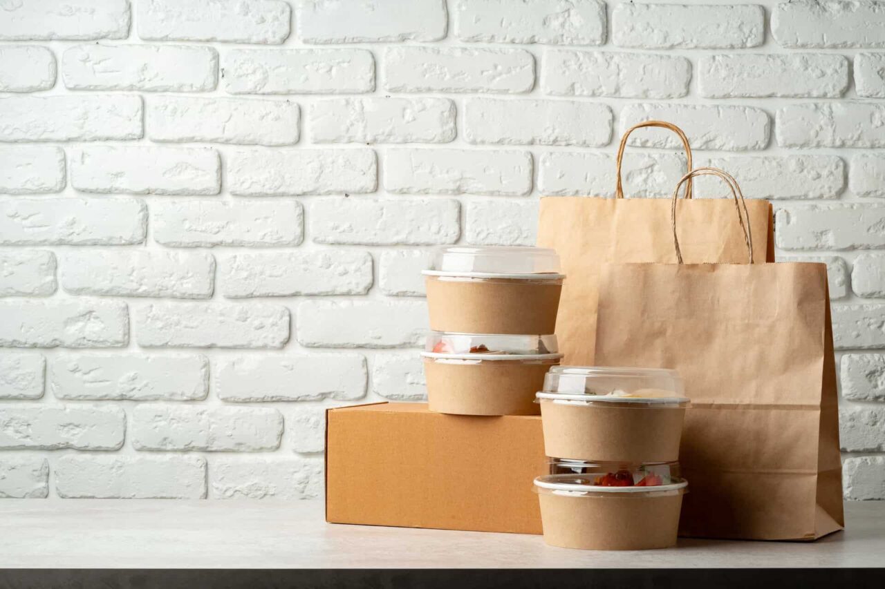 Takeout containers on a table with brown paper bags, illustrating trusted food service and distributors.