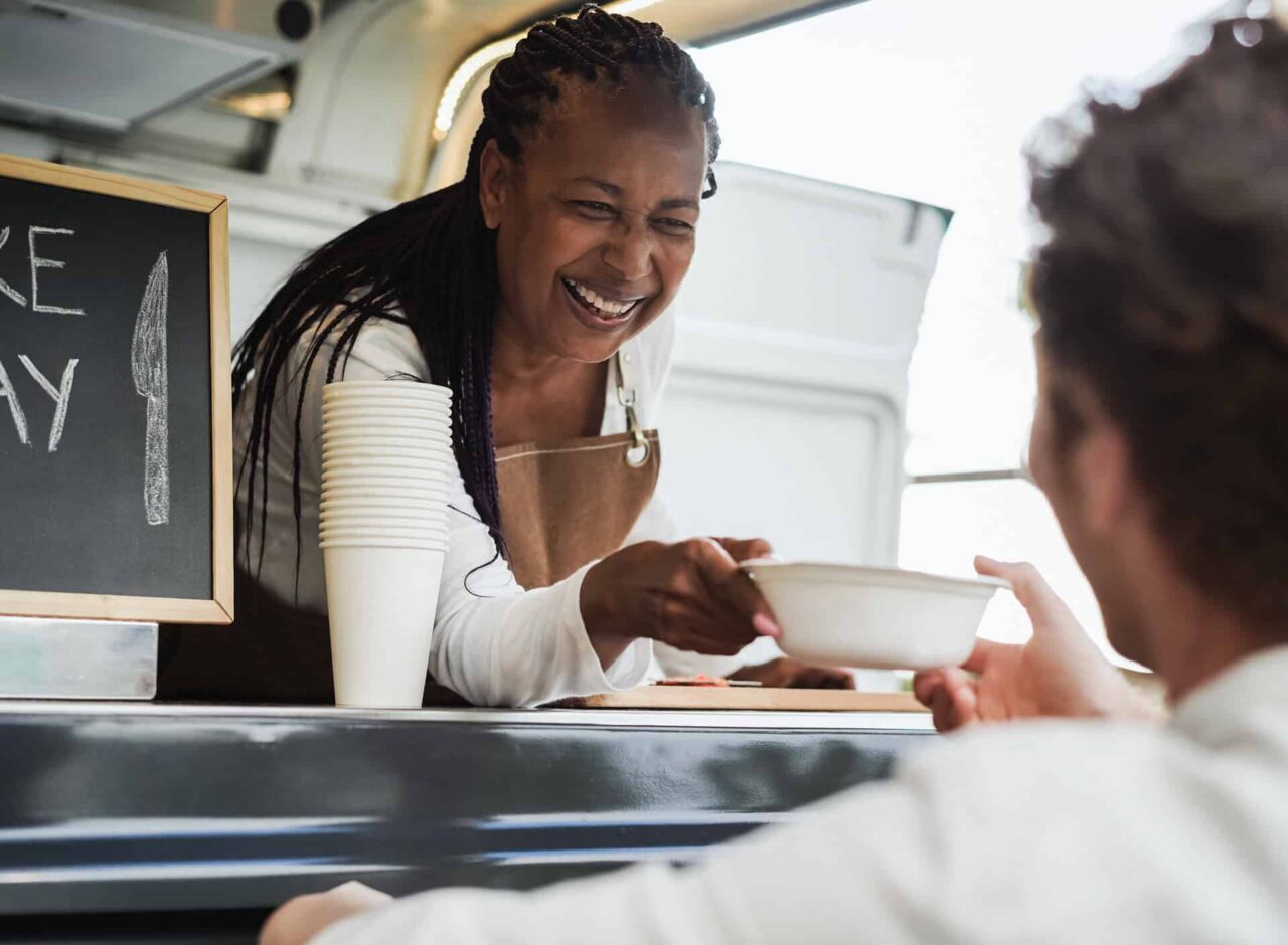 Smiling food service worker handing a dish to an end user, highlighting trusted disposable supplies through our network.