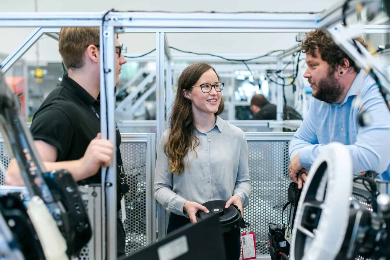 Three colleagues discussing inside a manufacturing facility, emphasizing teamwork and connection.