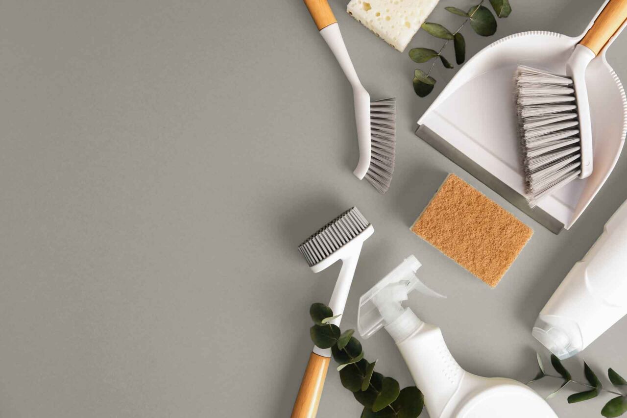 Cleaning supplies including brushes, spray bottle, sponge, and dustpan on a gray surface, highlighting janitorial solutions.