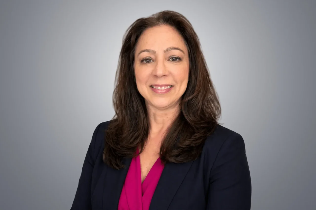 Professional woman smiling in a suit, symbolizing helping manufacturers and end users grow through connections.